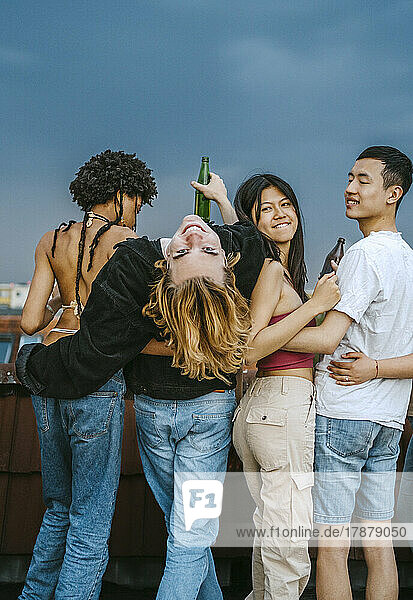 Portrait of young man bending backwards while standing amidst friends on rooftop