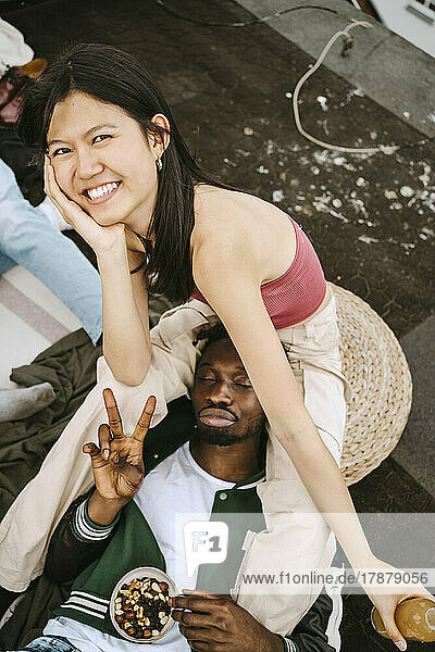 Porträt einer glücklichen jungen Frau mit einem männlichen Freund  der auf einer Dachterrassenparty das Friedenszeichen macht