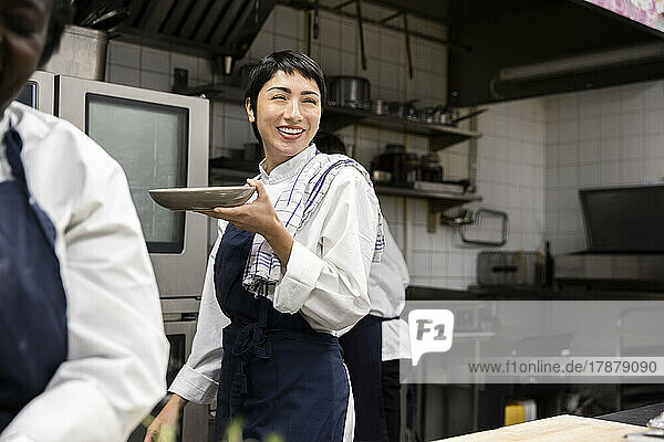 Smiling chef carrying plate while walking in restaurant kitchen