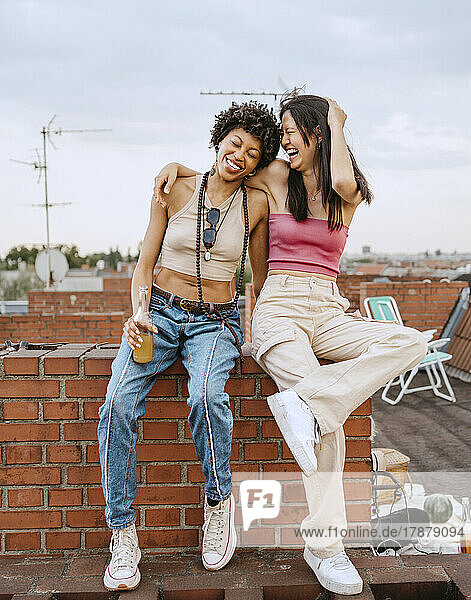 Full length of female friends laughing while sitting on rooftop