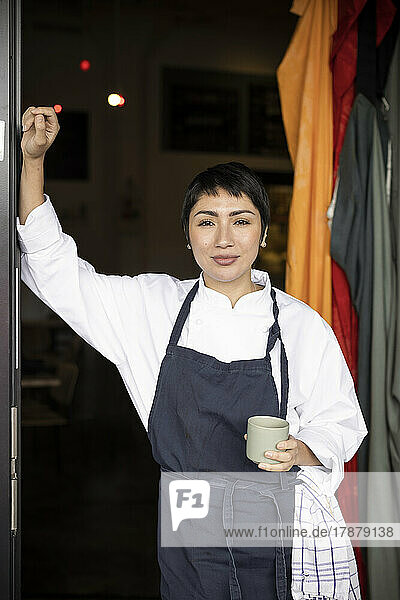 Portrait of restaurant owner holding cup while standing at entrance