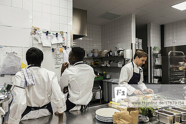 Multirassische Köche diskutieren am Whiteboard bei der Zubereitung von Speisen in einer Großküche
