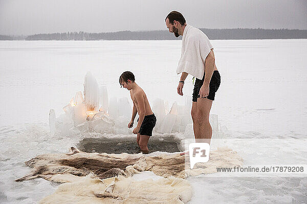 Seitenansicht eines reifen Mannes  der seinen Sohn beim Eisbaden auf einem zugefrorenen See beobachtet
