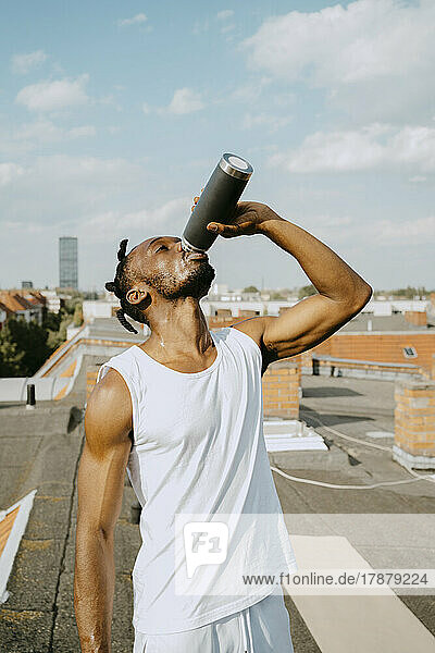 Young man drinking water from bottle on rooftop during sunny day
