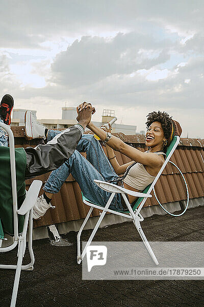 Fröhliche Frau in voller Länge  die die Hand eines männlichen Freundes hält  der auf einem Stuhl auf dem Dach sitzt