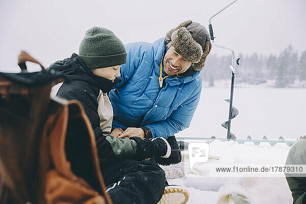 Happy father talking with son sitting on frozen lake
