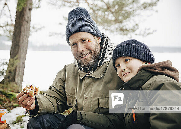 Lächelnder reifer Mann isst Hotdog mit Sohn im Winter
