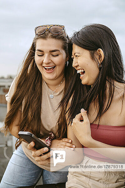 Junge Frauen lachen beim Teilen eines Smartphones