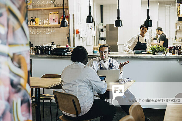 Chefkoch erklärt seinem Kollegen den Geschäftsplan  während er am Tisch im Restaurant sitzt