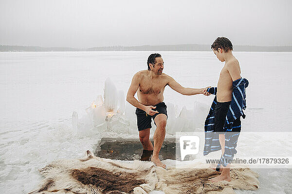Smiling man holding son's hand while coming out from ice bath