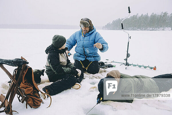 Happy man talking with son while friend fishing lying on snow