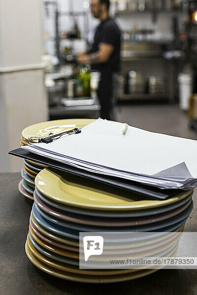 Clipboard on stack of plates on kitchen counter in restaurant