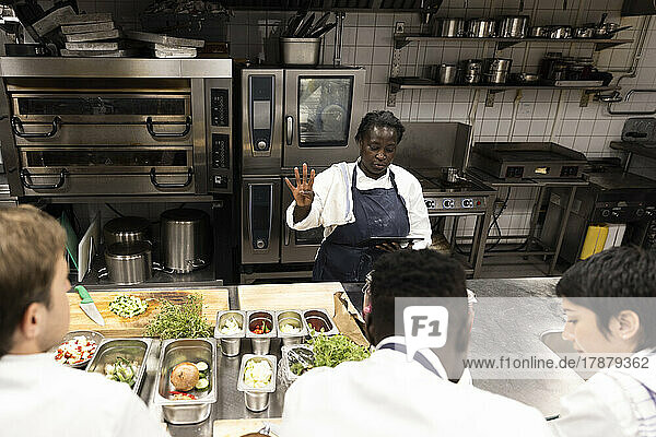Chef explaining strategy to colleagues while holding digital tablet in kitchen of restaurant