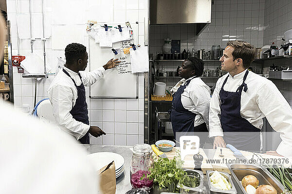 Männlicher Chefkoch erklärt seinen Kollegen am Whiteboard in der Küche eines Restaurants