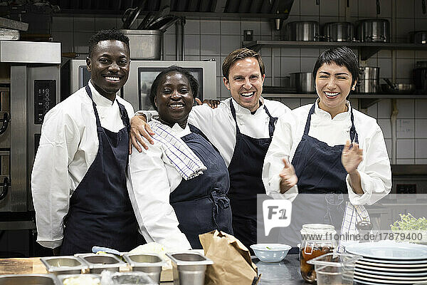 Portrait of happy multiracial colleagues standing in kitchen of restaurant