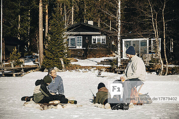 Smiling mature men with boys ice fishing on snow during sunny day