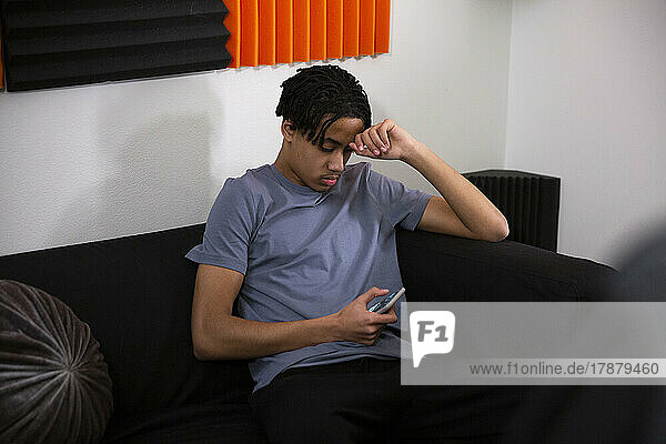 Teenage boy using smart phone while sitting on sofa in recording studio