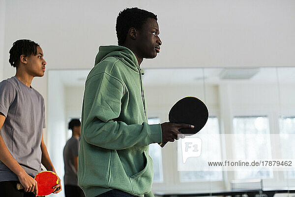 Man in green hoodie playing table tennis with friend in games room