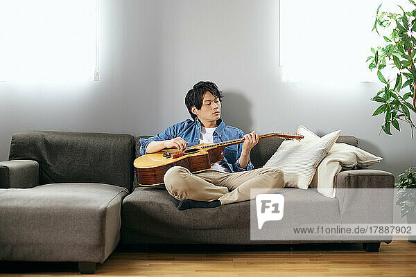 Japanese man playing guitar on the sofa