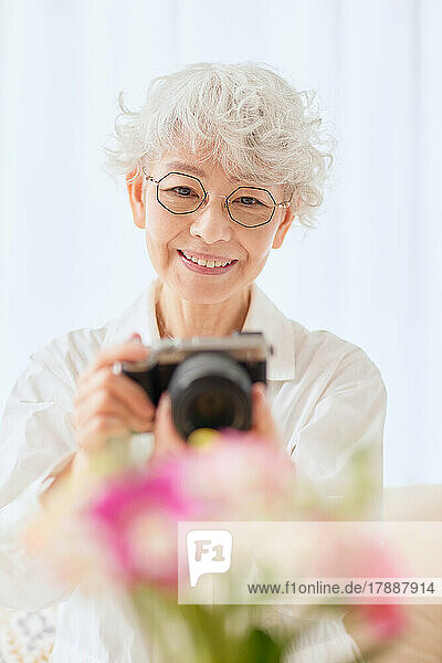 Japanische Seniorin  die auf dem Sofa Blumen fotografiert