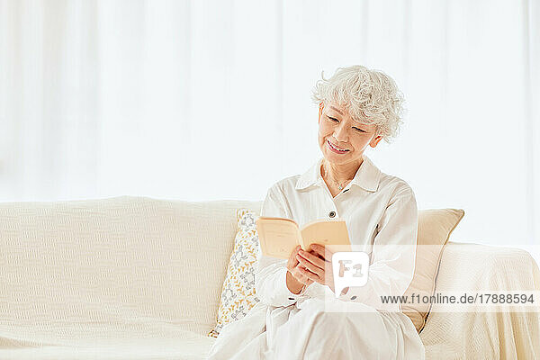 Japanische ältere Frau liest ein Buch auf dem Sofa
