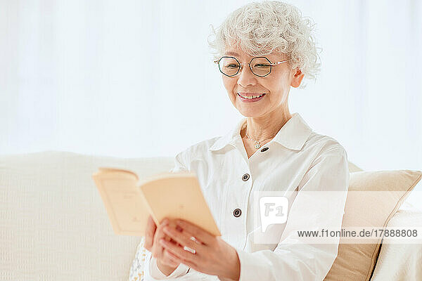 Japanische ältere Frau liest ein Buch auf dem Sofa