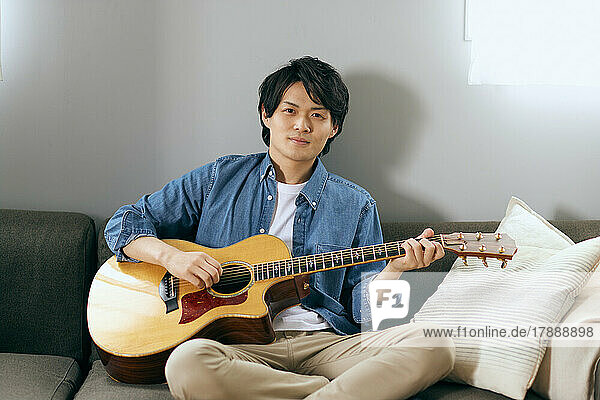Japanischer Mann spielt Gitarre auf dem Sofa