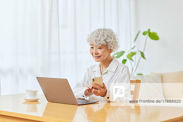Japanische Seniorin benutzt Laptop und Smartphone zu Hause