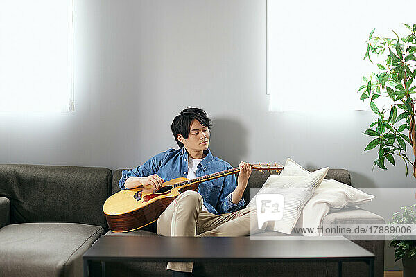 Japanese man playing guitar on the sofa