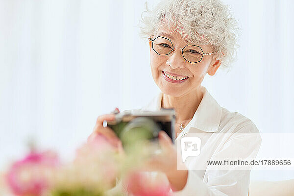 Japanese senior woman taking pictures of flowers on the sofa