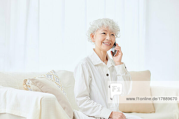 Japanische Seniorin mit Smartphone auf dem Sofa