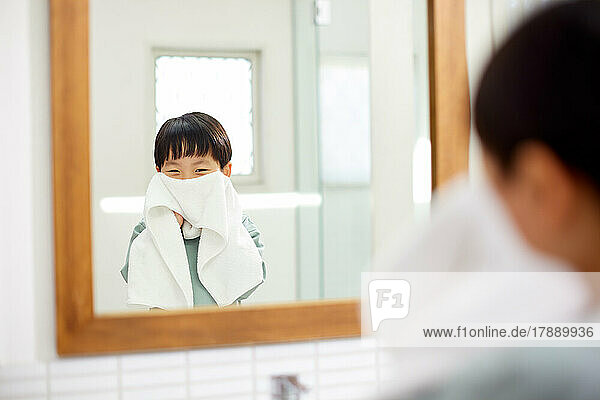 Japanisches Kind wischt sich zu Hause das Gesicht mit einem Handtuch ab