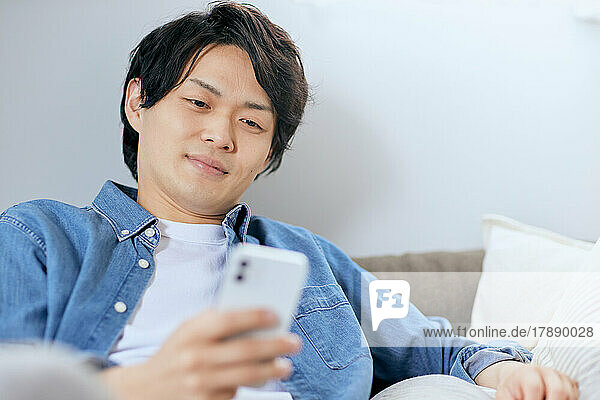 Japanischer Mann benutzt Smartphone auf dem Sofa