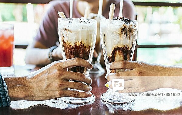 Mann und Frau Hand Toasting und hält zwei Milchshake. Zwei Hände stoßen mit Milchshake in einem Café an  Nahaufnahme von zwei Händen  die mit Eiskaffee in einem Café anstoßen