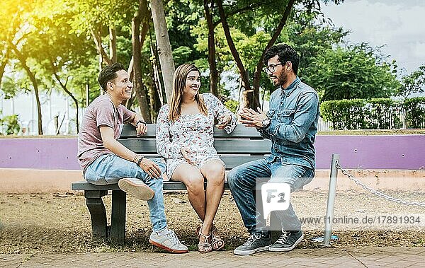 Three happy friends talking in a park. Three teenage friends talking sitting on a park bench  Group of three friends talking sitting in a park. Concept of people talking in the park