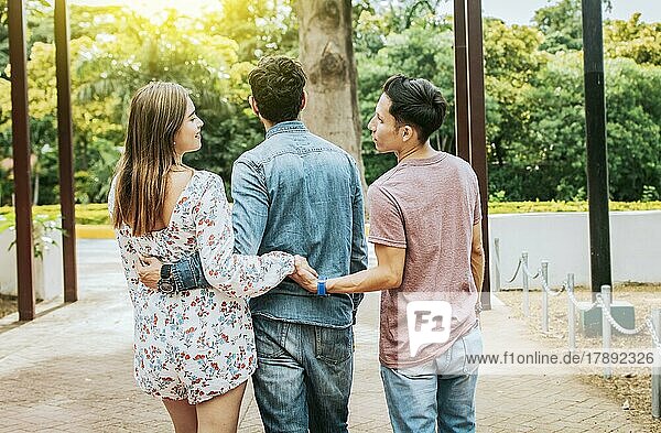 Unfaithful girl walking in the park with her boyfriend while holding another man hand. Love triangle concept. Woman holding hands with another man while walking with her boyfriend outdoor