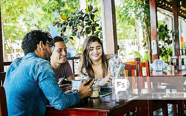 Junge Freunde in einem Café mit ihren Handys  die sich amüsieren. Drei Menschen in einem Café mit Handys  die sich amüsieren. Drei Teenager-Freunde mit ihren Handys in einem Café