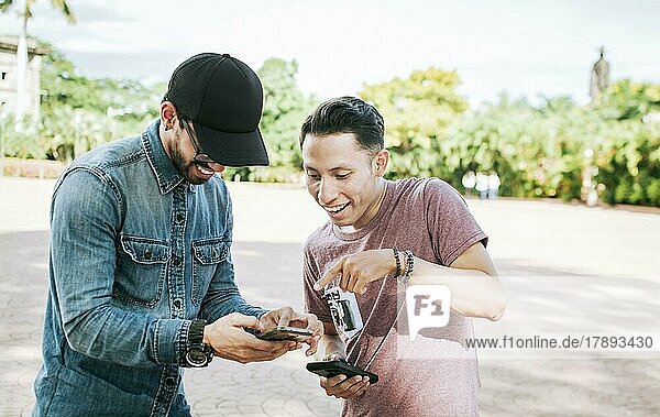 Zwei glückliche Freunde  die ein Handy auf der Straße betrachten  Zwei lächelnde Freunde  die Medien auf dem Handy auf der Straße betrachten  Zwei junge Freunde  die Spaß mit dem Handy im Freien haben