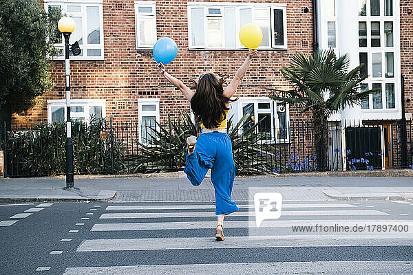 Sorglose Frau mit Luftballons läuft auf Zebrastreifen in der Stadt