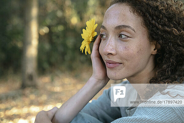 Nachdenkliche junge Frau mit gelber Blume im Park