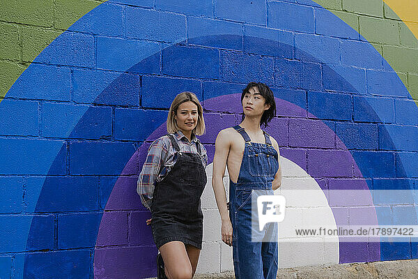 Friends standing by rainbow painted on wall