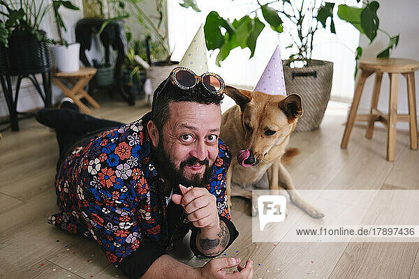 Smiling man eating sausage by pet dog at home