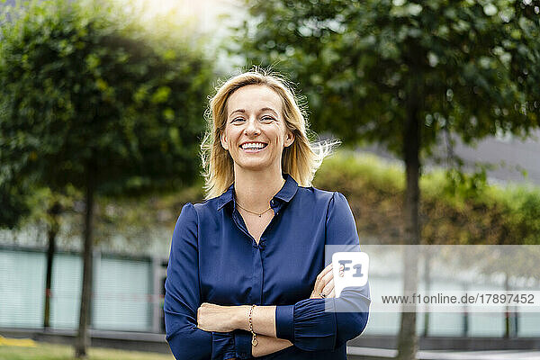 Smiling businesswoman with arms crossed standing at park