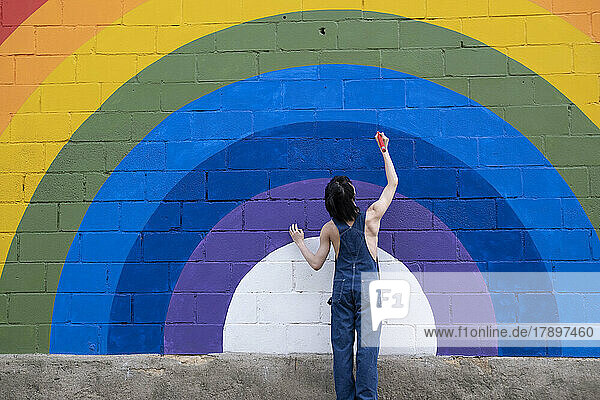 Young man drawing with pencil on rainbow mural