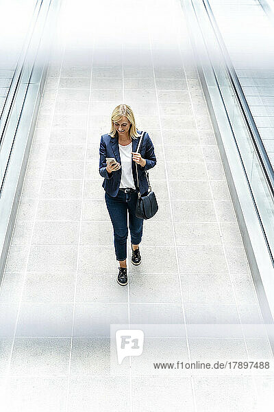 Smiling businesswoman using phone walking on walkway