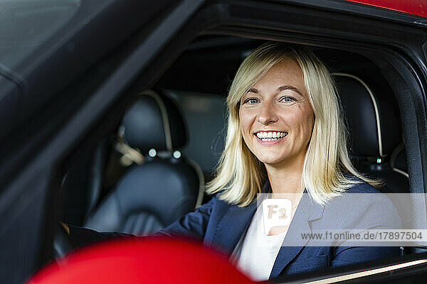 Happy businesswoman with blond hair sitting in car