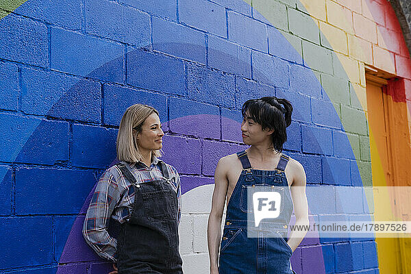 Young man and woman standing by rainbow painted on wall