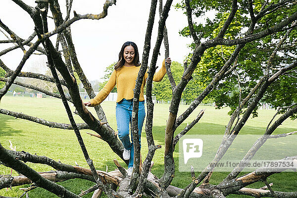 Playful young woman walking on fallen tree in park