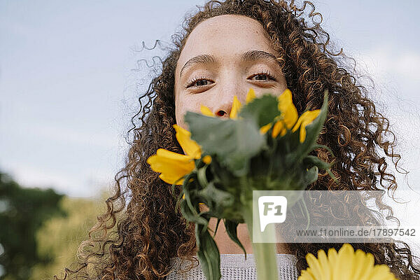 Junge Frau hält Sonnenblume vor Gesicht