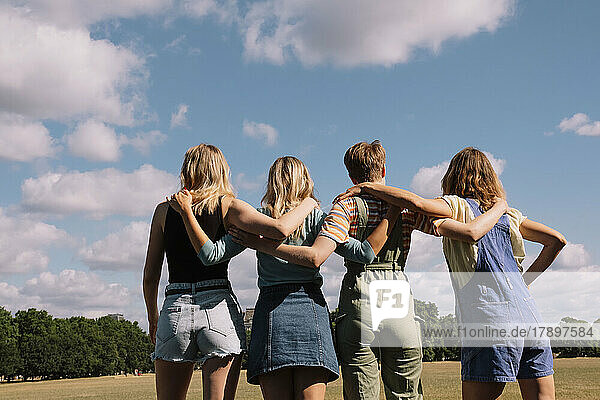 Friends with arms around standing under cloudy sky